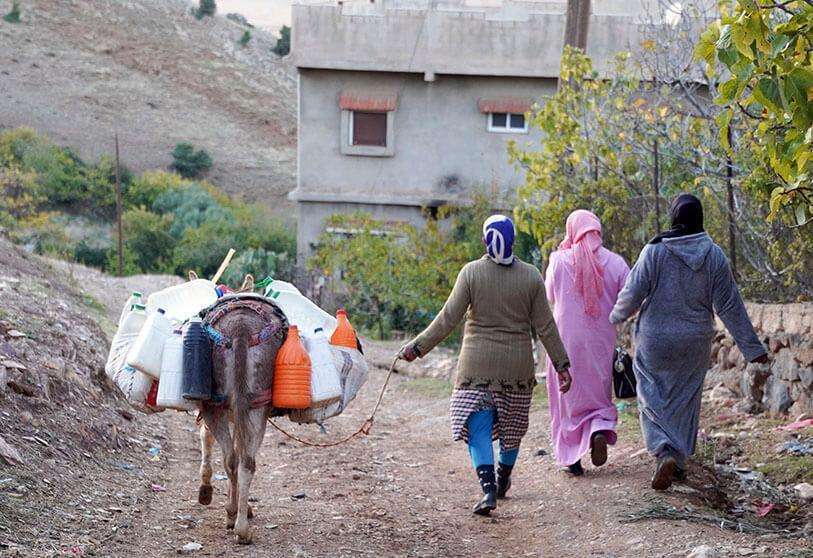 PHOTO/REUTERS - Tres mujeres caminan con su burro llevando recipientes de plástico con agua a sus casas a las afueras de Azrou, en Marruecos