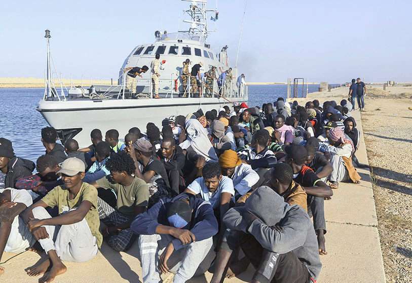 Migrantes rescatados sentados junto a un barco de la Guardia Costera en la ciudad de Khoms, Libia