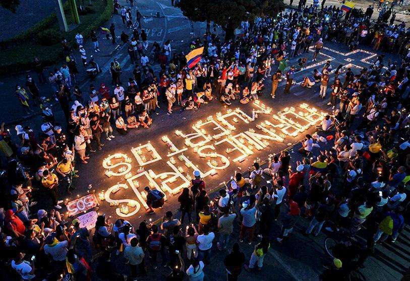 AFP/LUIS ROBAYO - Colombianos se reúnen alrededor de velas y palabras en el pavimento que dicen "por nuestros muertos" durante una vigilia el 5 de mayo de 2021 en Cali, Colombia, en honor a los manifestantes que murieron durante las protestas contra el gobierno del presidente Iván Duque