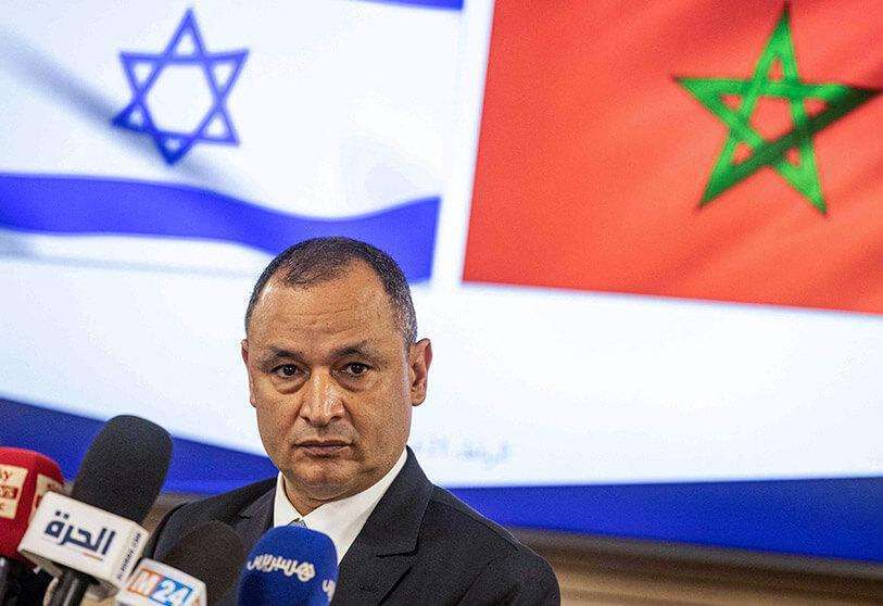 AFP/FADEL SENNA - El ministro marroquí de Industria y Comercio, Ryad Mezzour, se dirige a los medios de comunicación bajo las banderas de su país y de Israel (izq.)